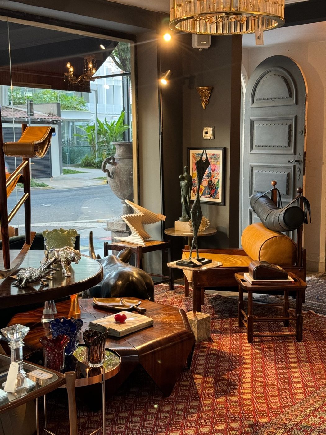 Salão da loja com mesa de jacarandá, vidros de Murano, escultura em bronze e lustre de cristal