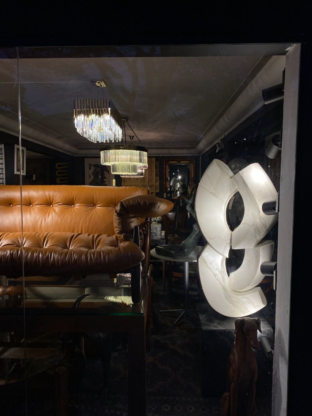 Vitrine à noite com lustres de cristal, sofá de couro e escultura em mármore